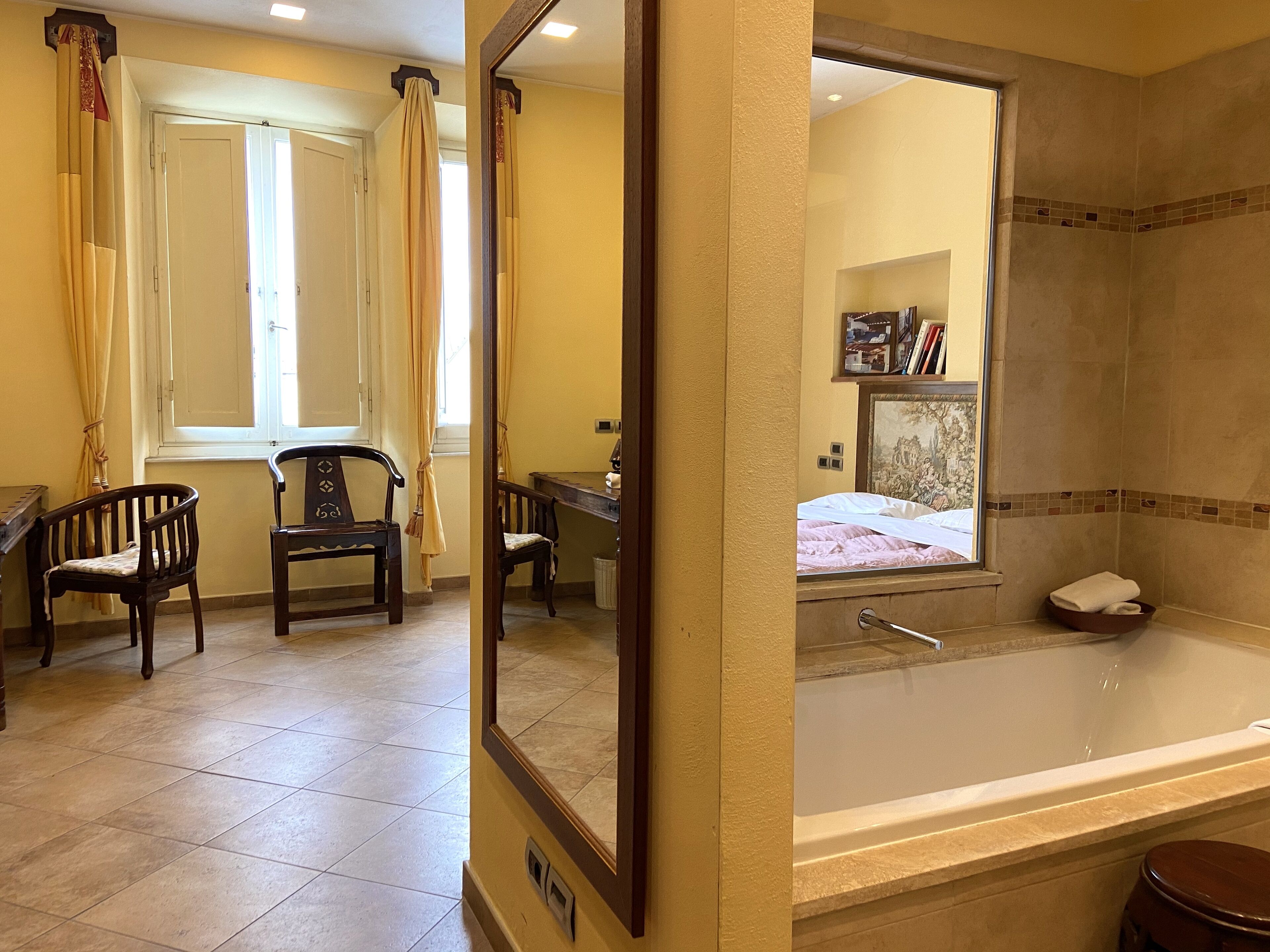 A hotel room with a large bed, a bathtub, and two wooden chairs.