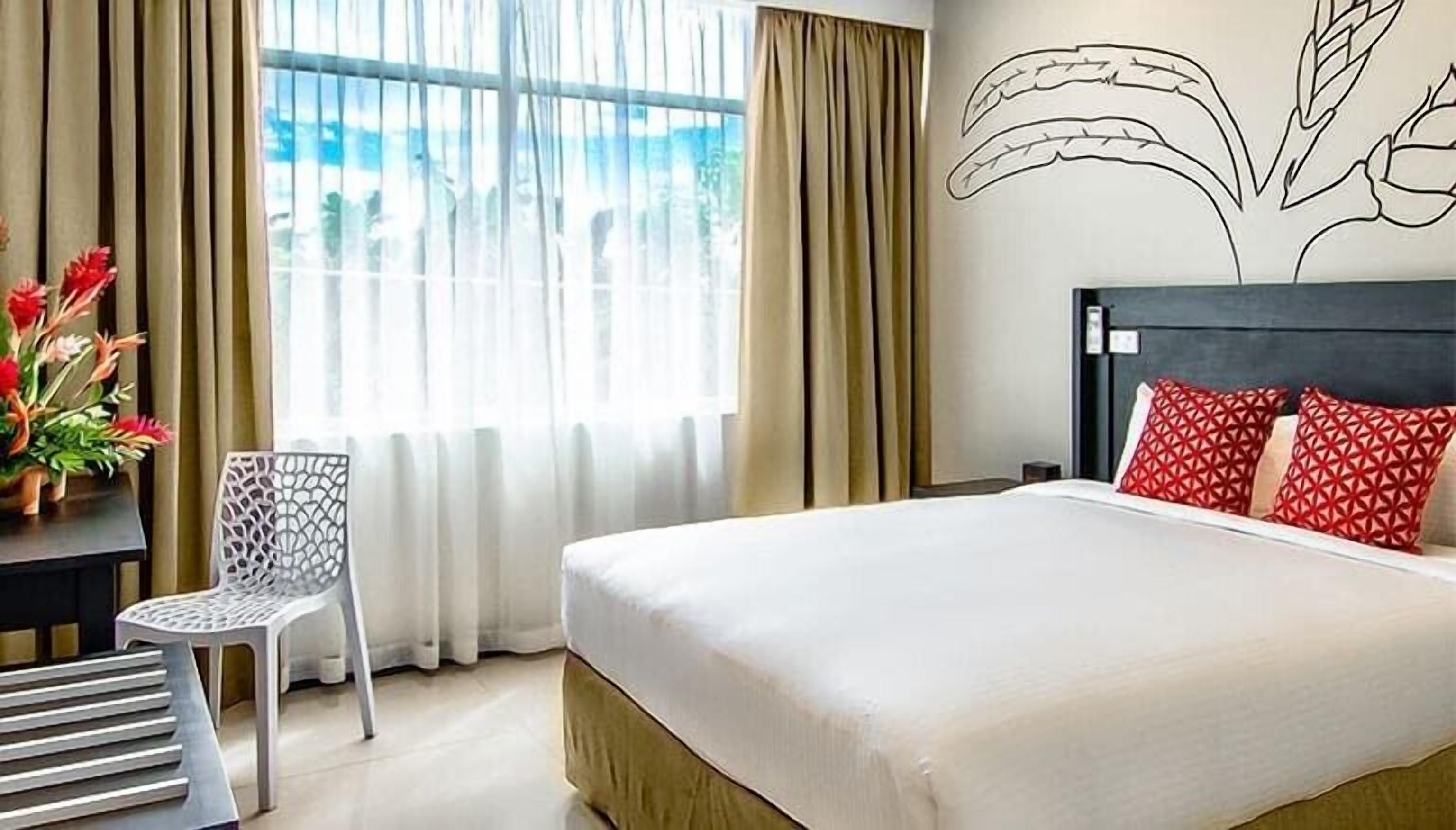 A hotel room with a bed, a desk with a chair, and a window with curtains.