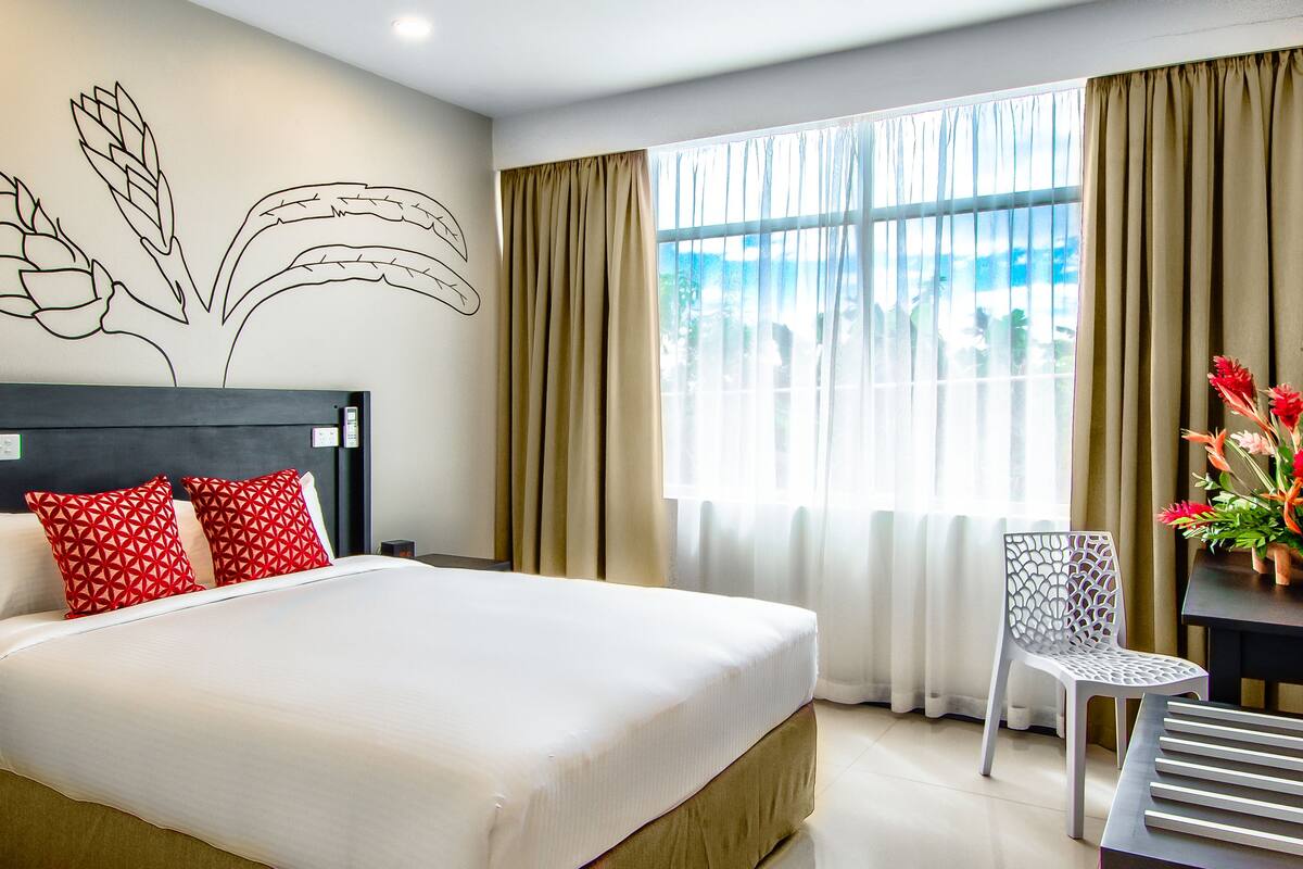 A hotel room with a large bed, a desk with a chair, a TV, and a window with curtains.