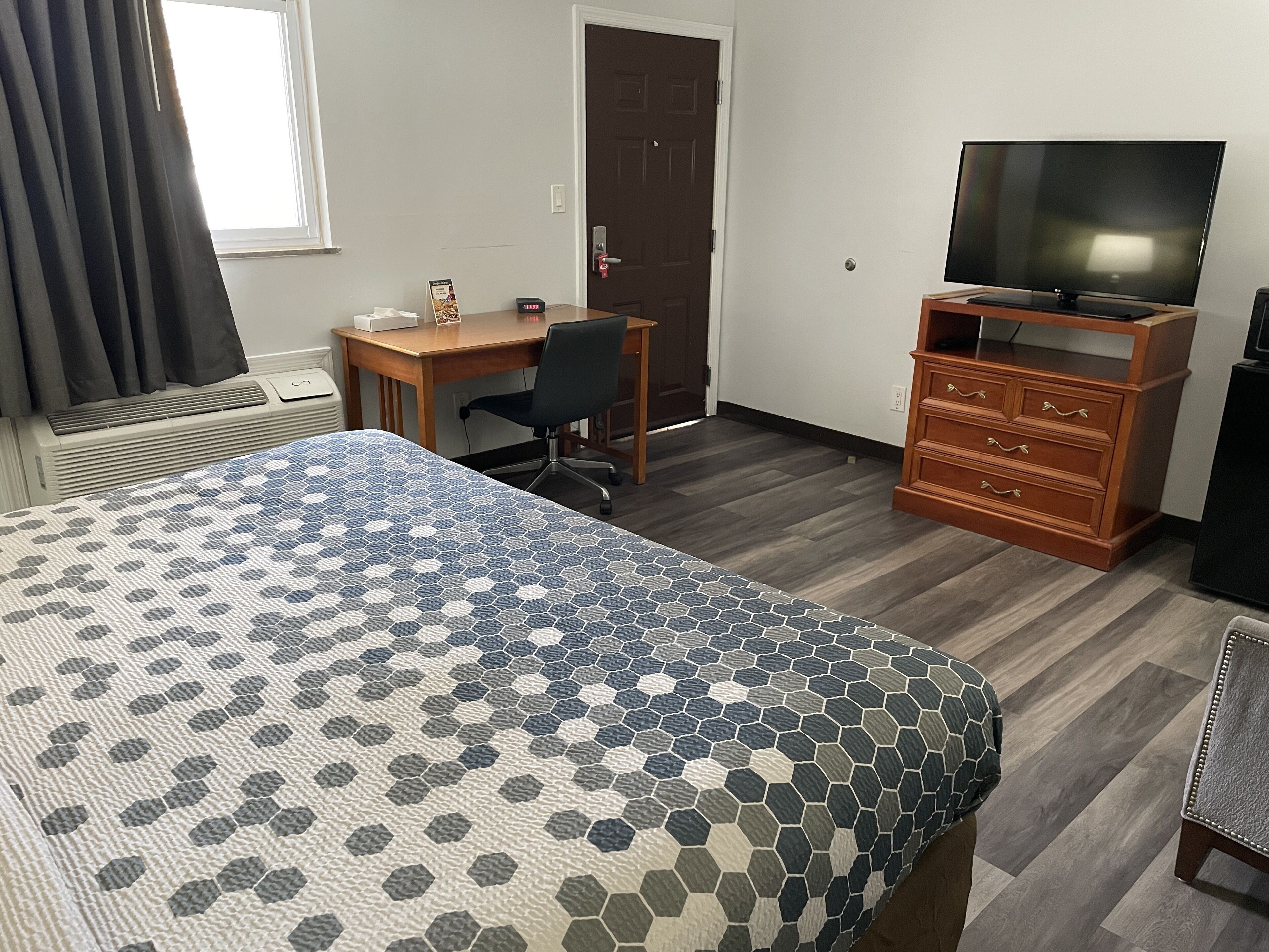 Una habitación de hotel con una cama, un escritorio, una silla, un televisor y un aparador.