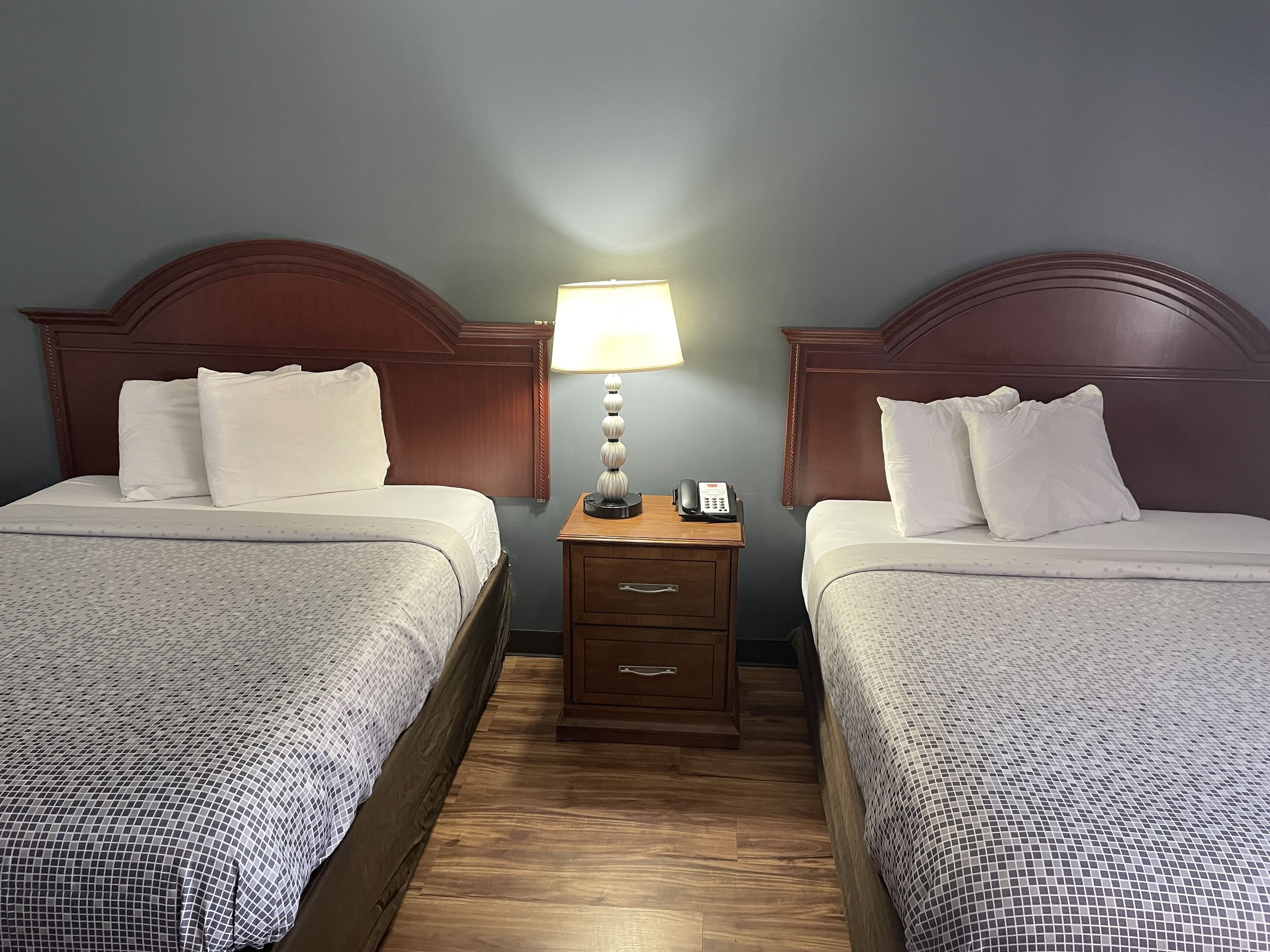 A hotel room with two beds, a nightstand with a lamp, and a phone.