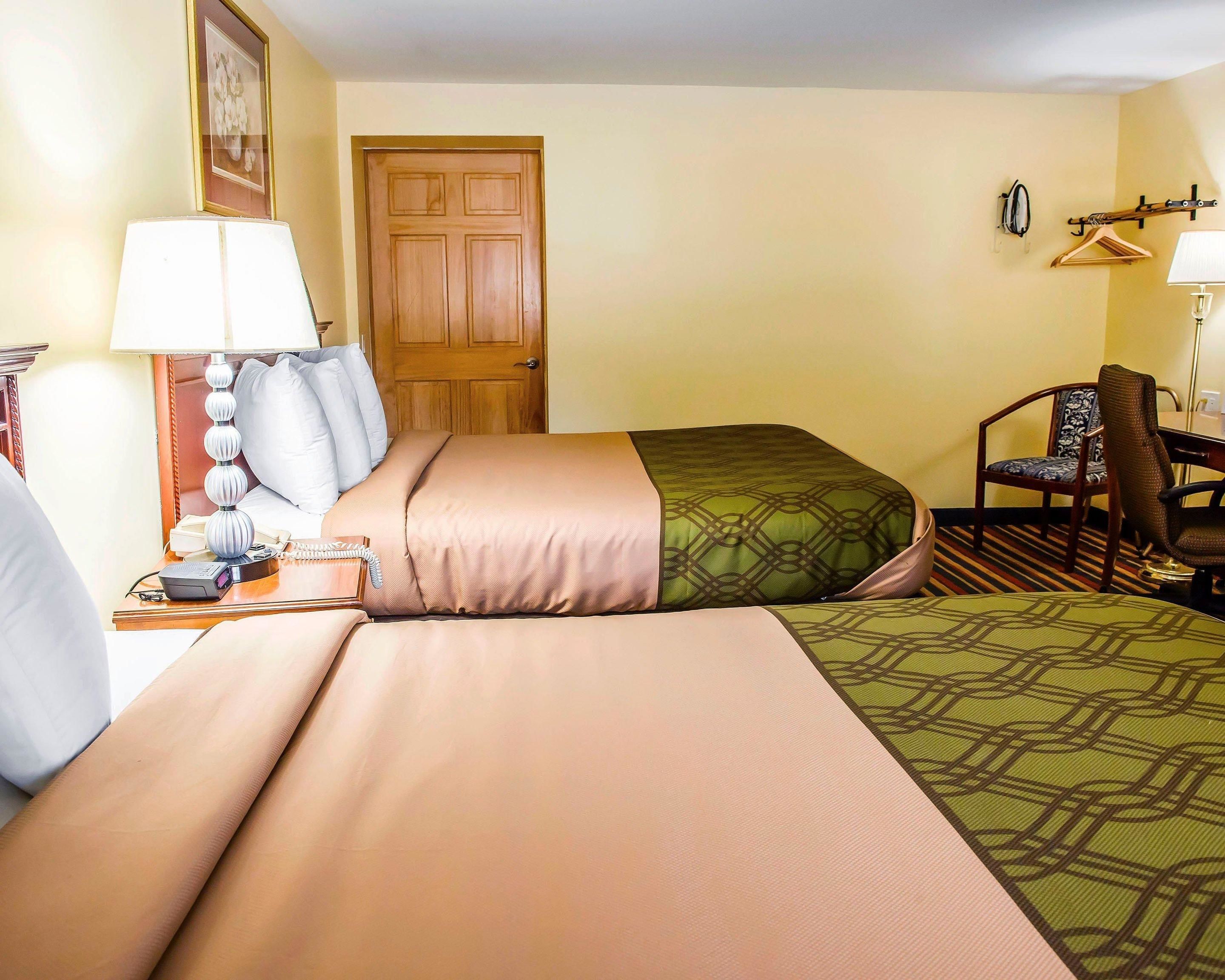 A hotel room with two beds, a desk, a chair, a lamp, and a door.