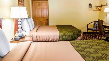 A hotel room with two beds, a desk, a chair, a lamp, and a door.