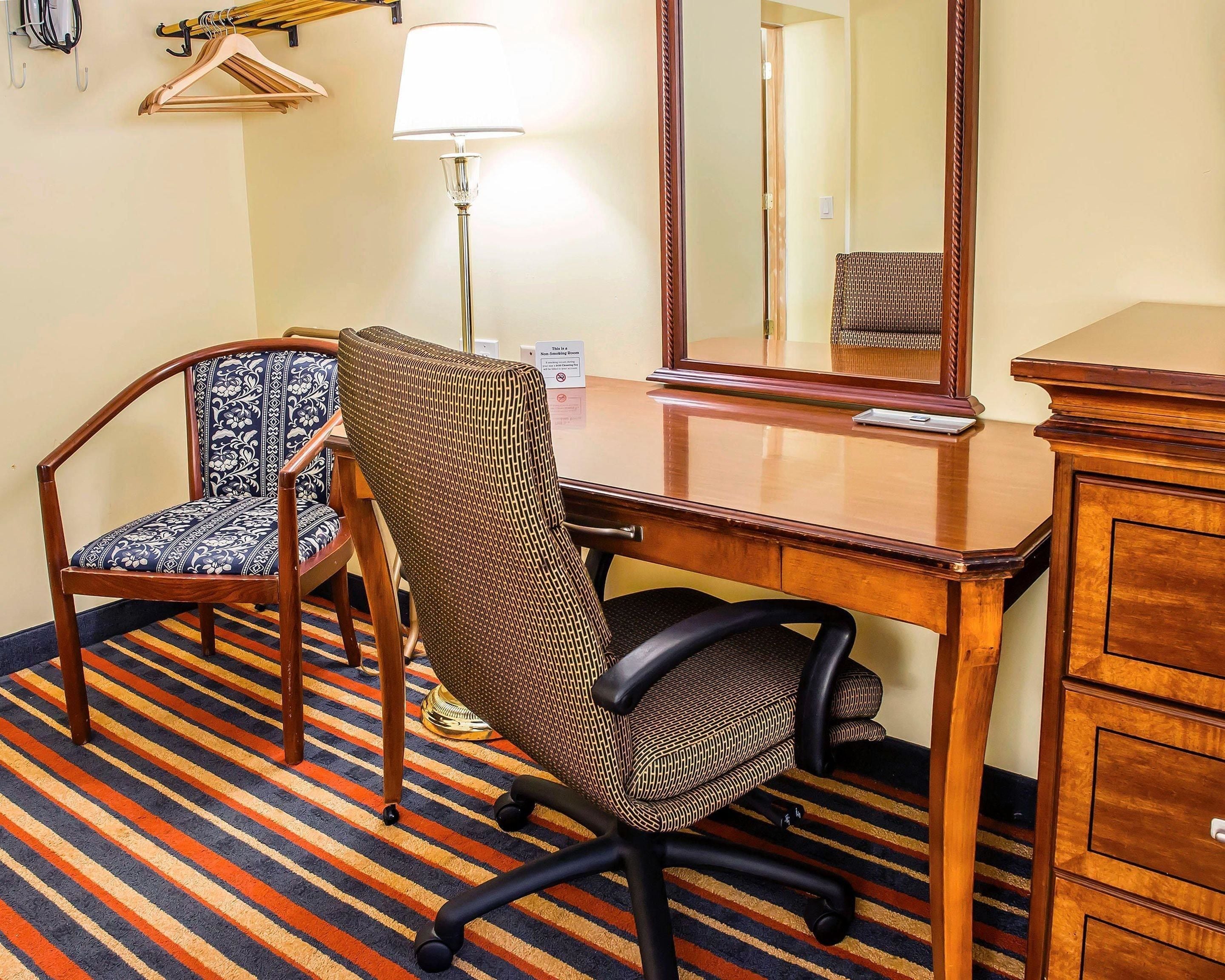 Een hotelkamer met een houten bureau, twee stoelen, een spiegel, een lamp en een gestreept tapijt.