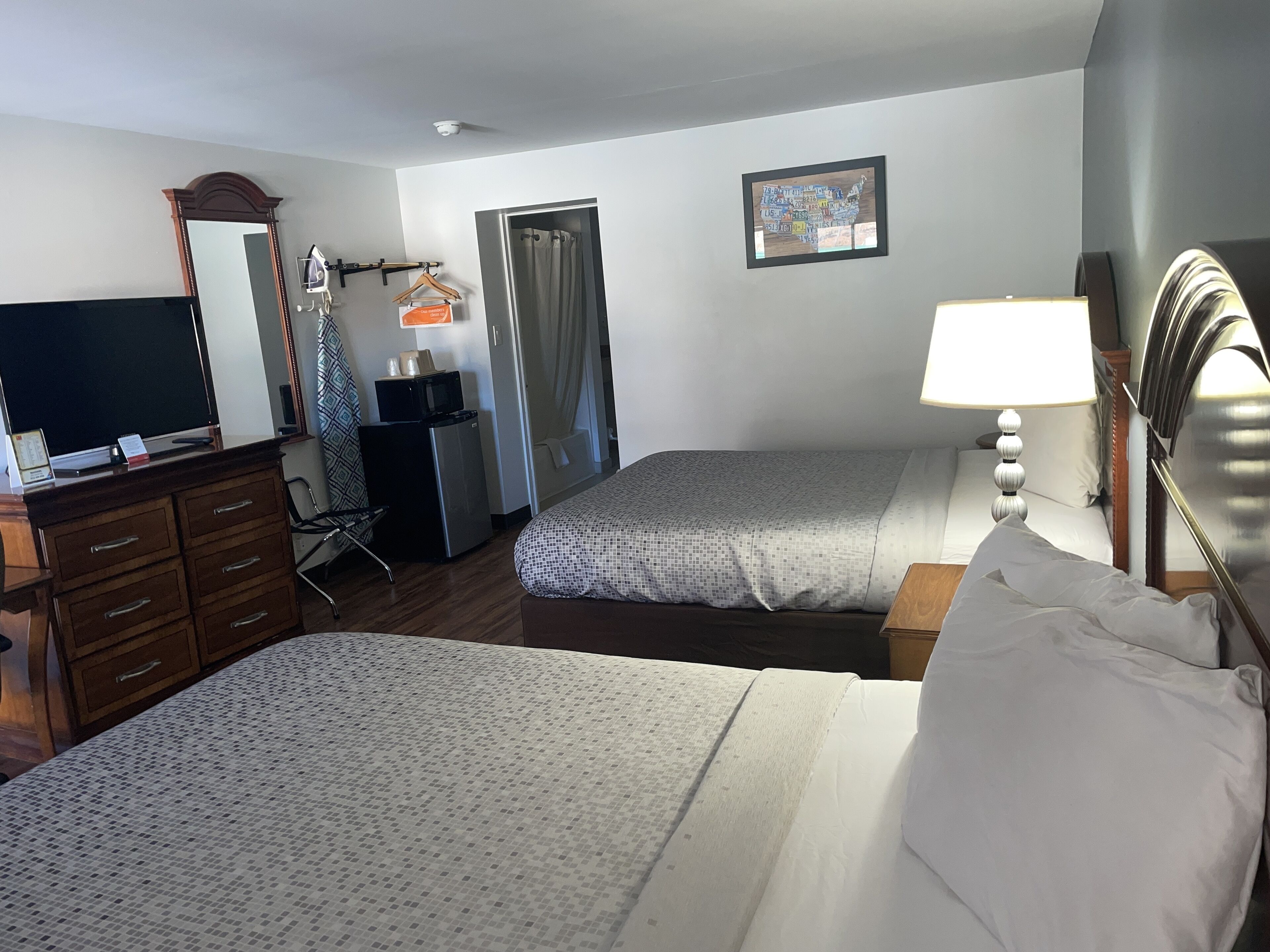 Ein Hotelzimmer mit zwei Betten, einem Schreibtisch mit Flachbildfernseher, einem Schminktisch, einer Mikrowelle und einer Tür zu einem Badezimmer.