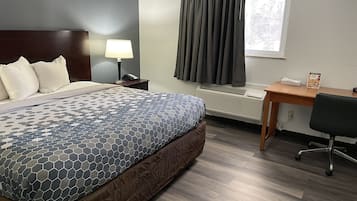 A hotel room with a bed, a desk, a chair, a lamp, a telephone, a window with curtains, and an air conditioning unit.