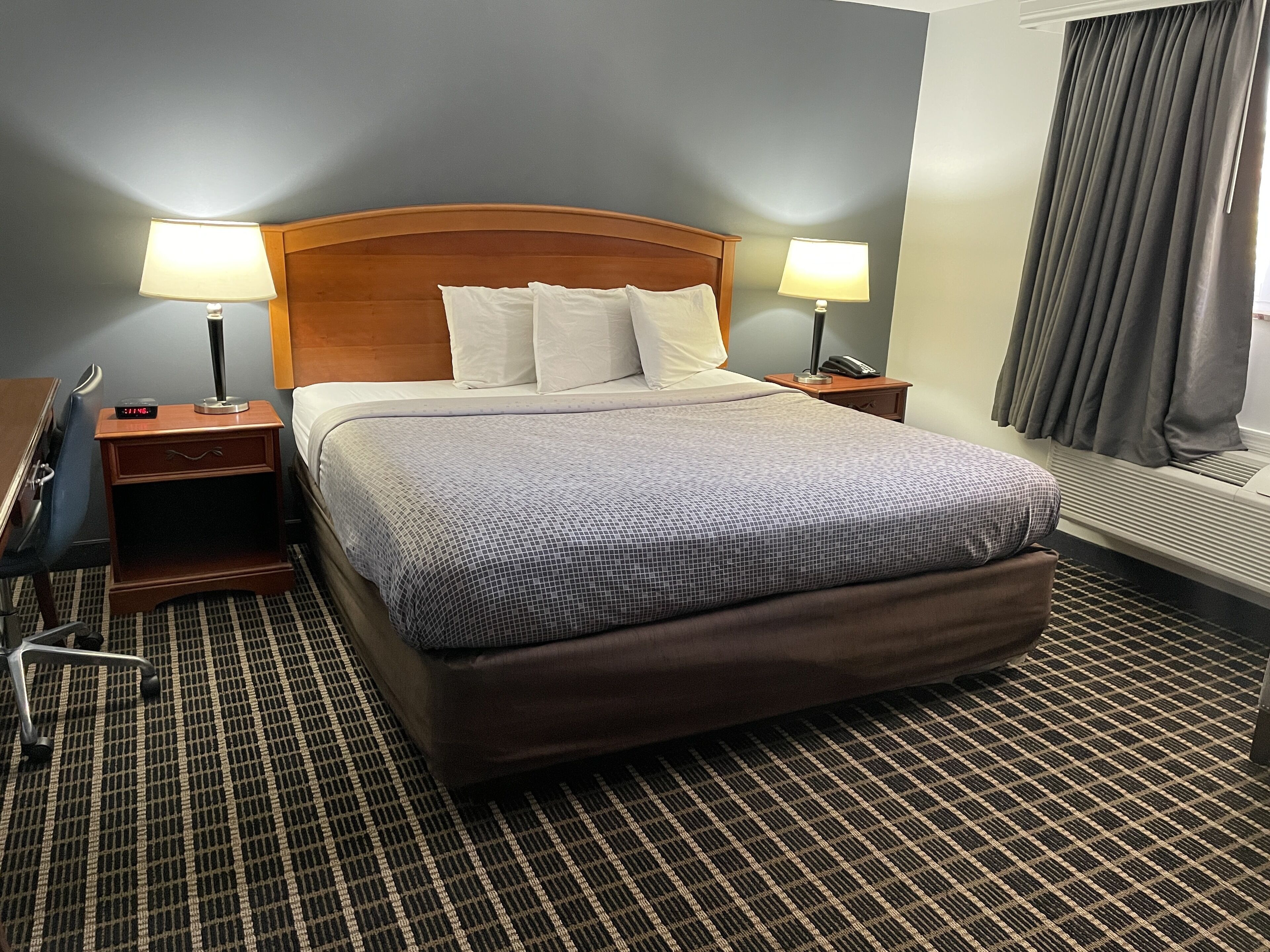 A hotel room with a large bed, two bedside tables with lamps, a desk, and a chair.