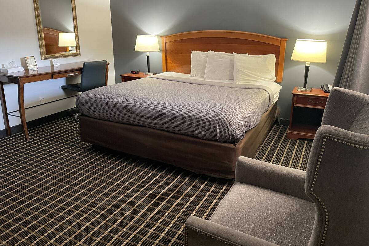 Habitación de hotel con una cama grande, dos mesitas de noche con lámparas, un escritorio con una silla, un espejo amplio y un suelo a cuadros.