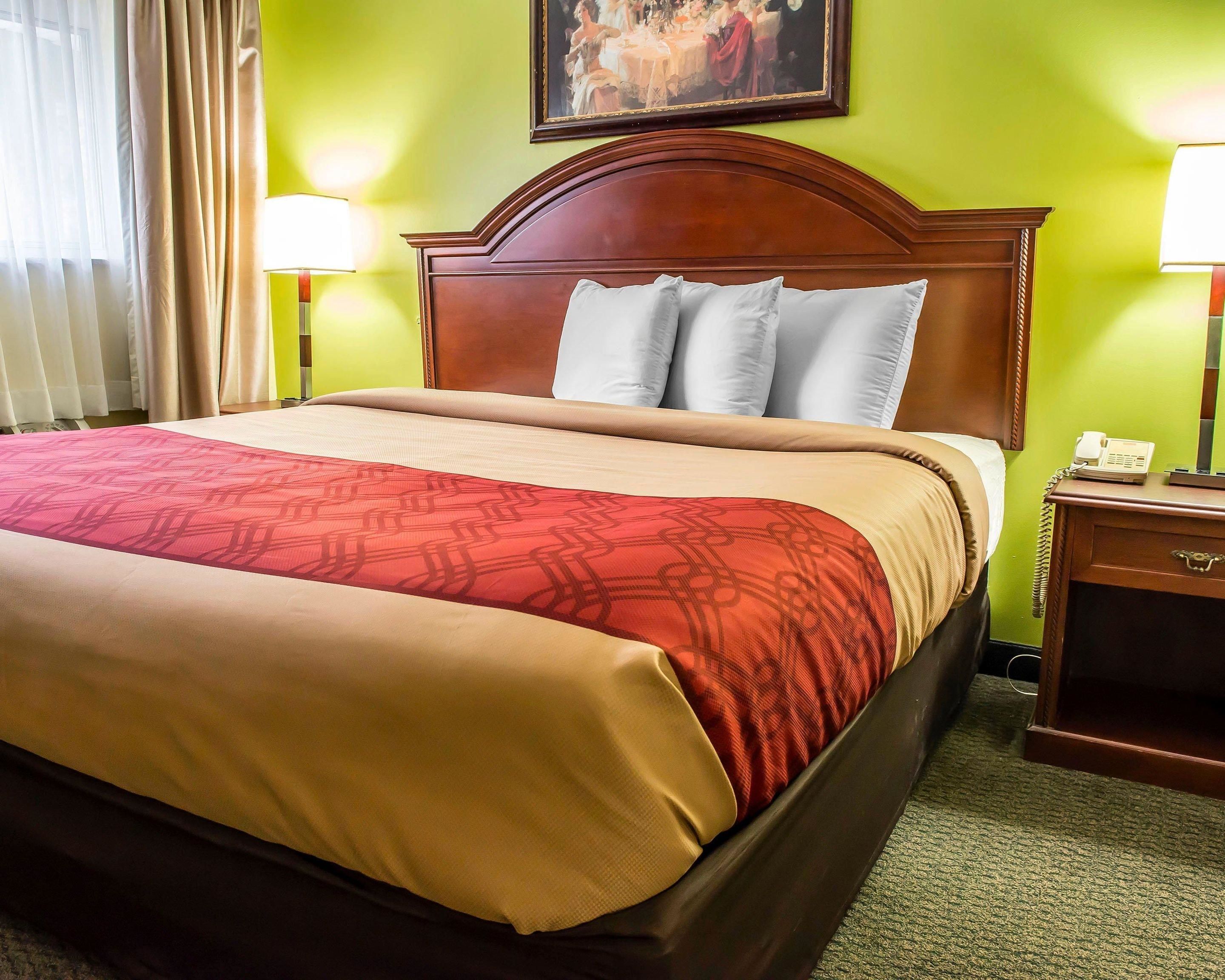 A hotel room with a large bed, a wooden headboard, two bedside lamps, and a painting on the wall.
