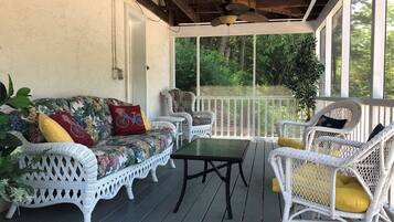 Relax on the covered porch with a sofa, chairs, and a small table, surrounded by lush greenery through the large window.