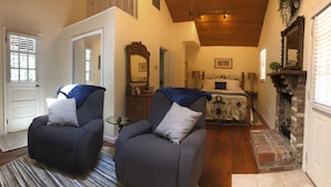 A cozy room with two armchairs, a bed with a headboard, a mirror, and a fireplace. - Jackson House B&B (Railroad)