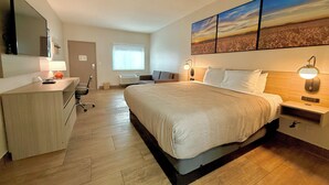 A hotel room with a bed, desk, chair, and artwork on the wall.