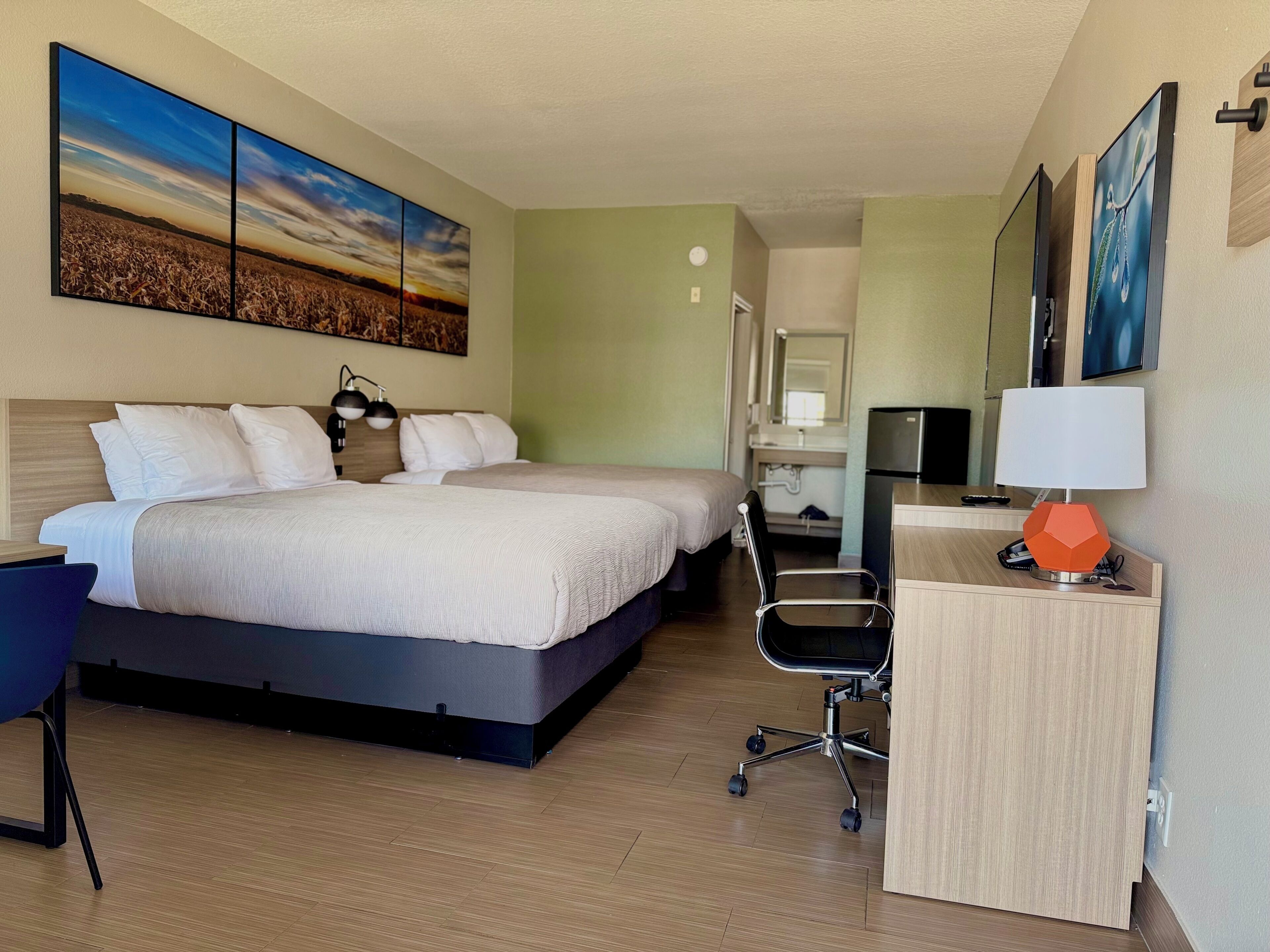 A hotel room with a bed, desk, chair, and a large painting on the wall.