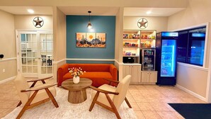 A living room with a sofa, coffee table, and chairs, a kitchen area with a refrigerator and pantry, and a dining area with a table and chairs.