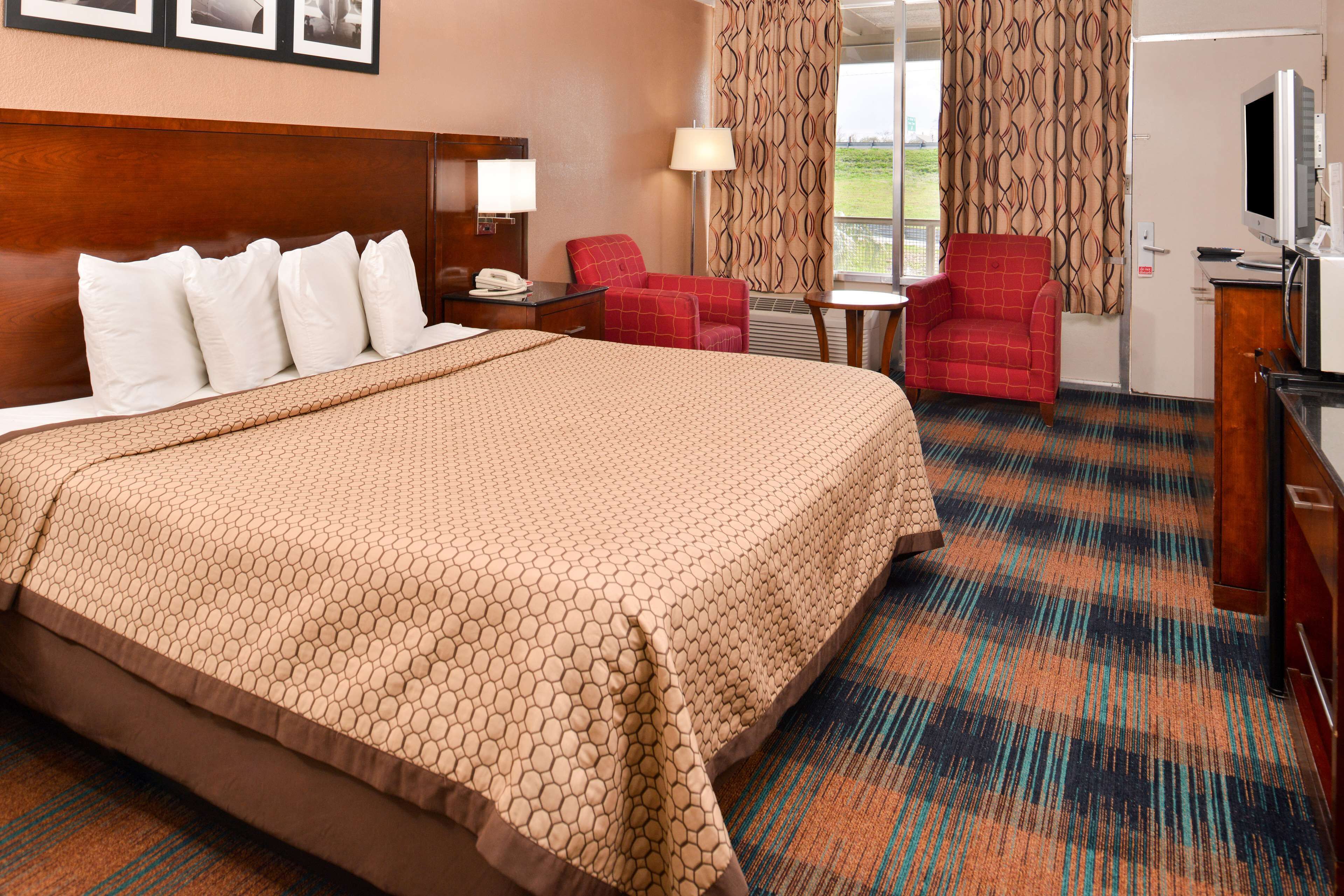 A hotel room with a large bed, a desk with a lamp, a television, and a red armchair.