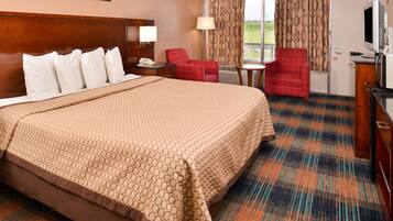 A hotel room with a large bed, a desk with a lamp, a television, and a red armchair.