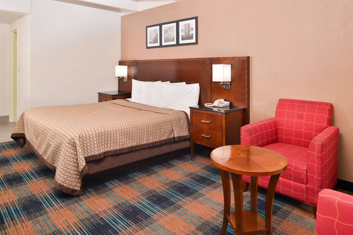 Une chambre d’hôtel avec un lit, une table de chevet, une lampe et un fauteuil rouge.