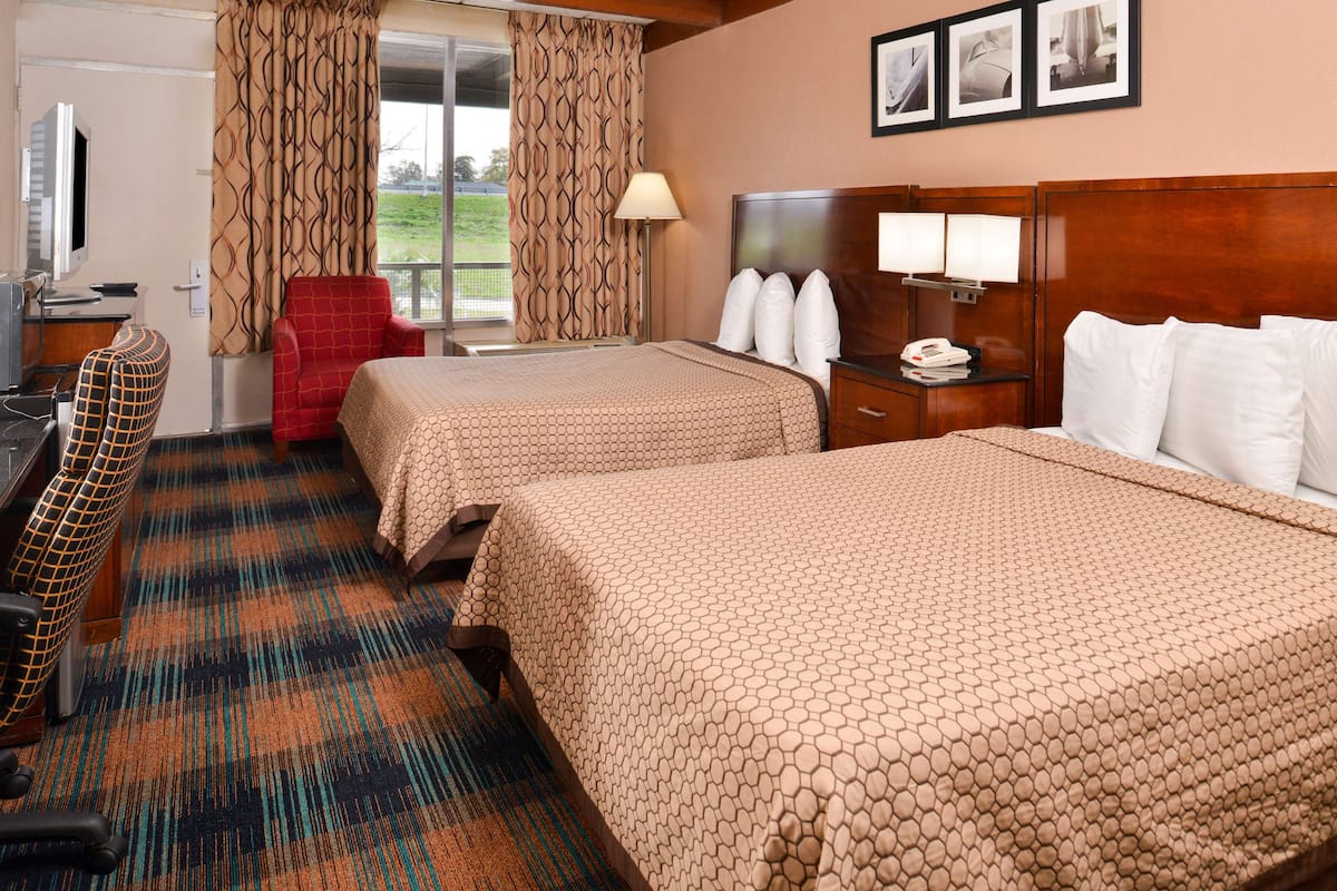 Une chambre d’hôtel avec deux lits, un bureau, une chaise et une télévision.
