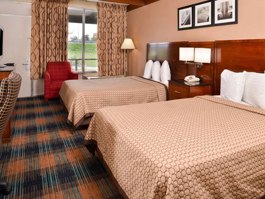 Habitación de hotel con dos camas, un escritorio, una silla y un televisor.