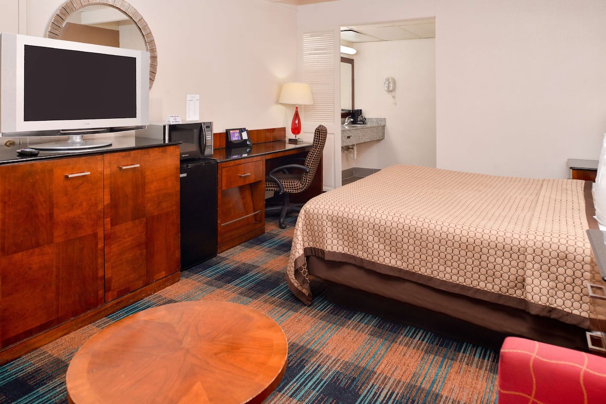 Une chambre d’hôtel comprenant un lit, un bureau avec un ordinateur, une télévision, une chaise, une table et un miroir.