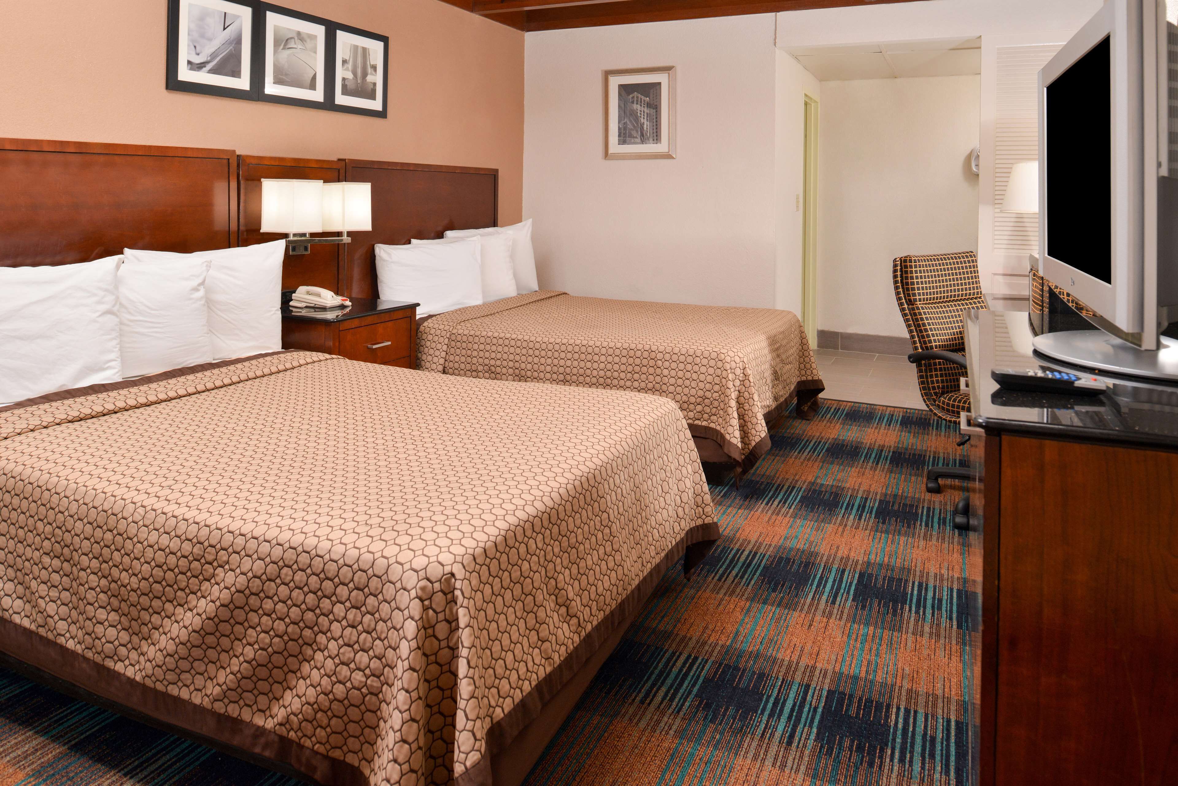 A hotel room with two beds, a television, a desk with a lamp, and a chair.