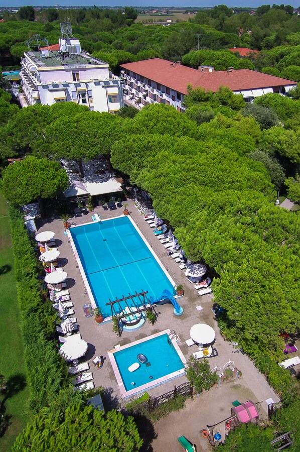 Vista aérea de una piscina rodeada de exuberante vegetación, con un edificio al fondo.