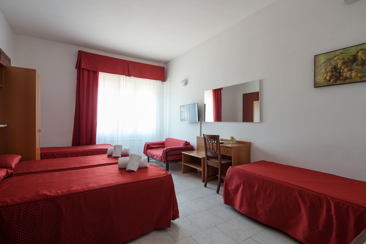 Una habitación de hotel con dos camas individuales, un escritorio, una silla, un televisor y una ventana con cortinas.