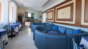 Un espacio interior amplio con un sofá grande azul, varias mesas con manteles azul y blanco, y un piso de baldosas.