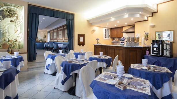 Un restaurante con mesas dispuestas para comer, una zona de bar y una cocina visible al fondo.