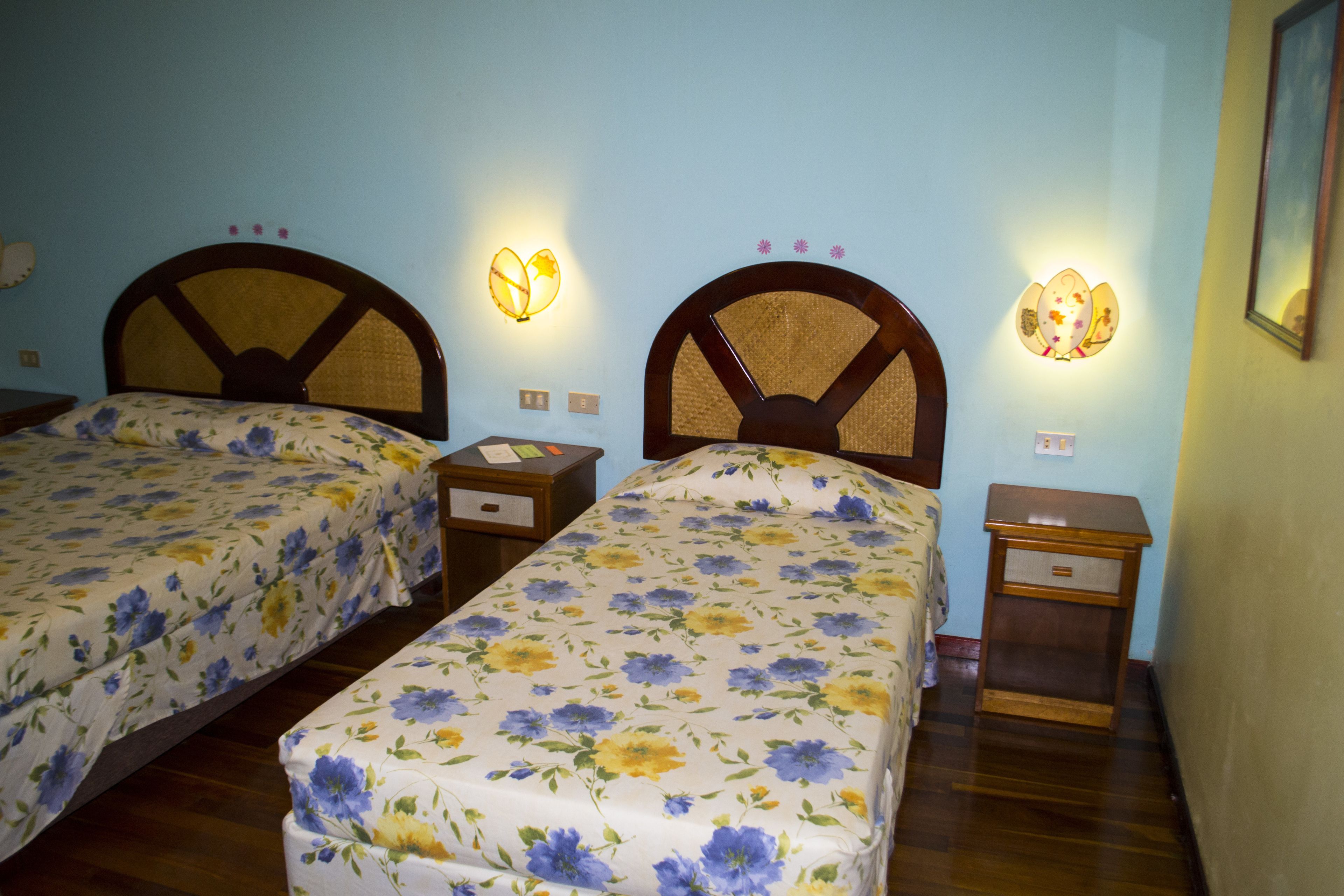 Dos camas individuales con ropa de cama floral, cabeceros de madera, mesitas de noche y lámparas de pared.