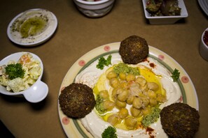 A plate of hummus with chickpeas and falafel, garnished with parsley, on a table with other dishes.