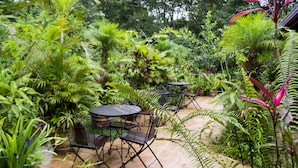 A patio area with a round table and chairs, surrounded by various potted plants and greenery.