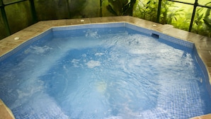 A hot tub with a tiled edge and a view of green plants through the window.
