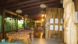 A wooden-floored room with a foosball table, a large wooden statue, and framed botanical prints on the wall.