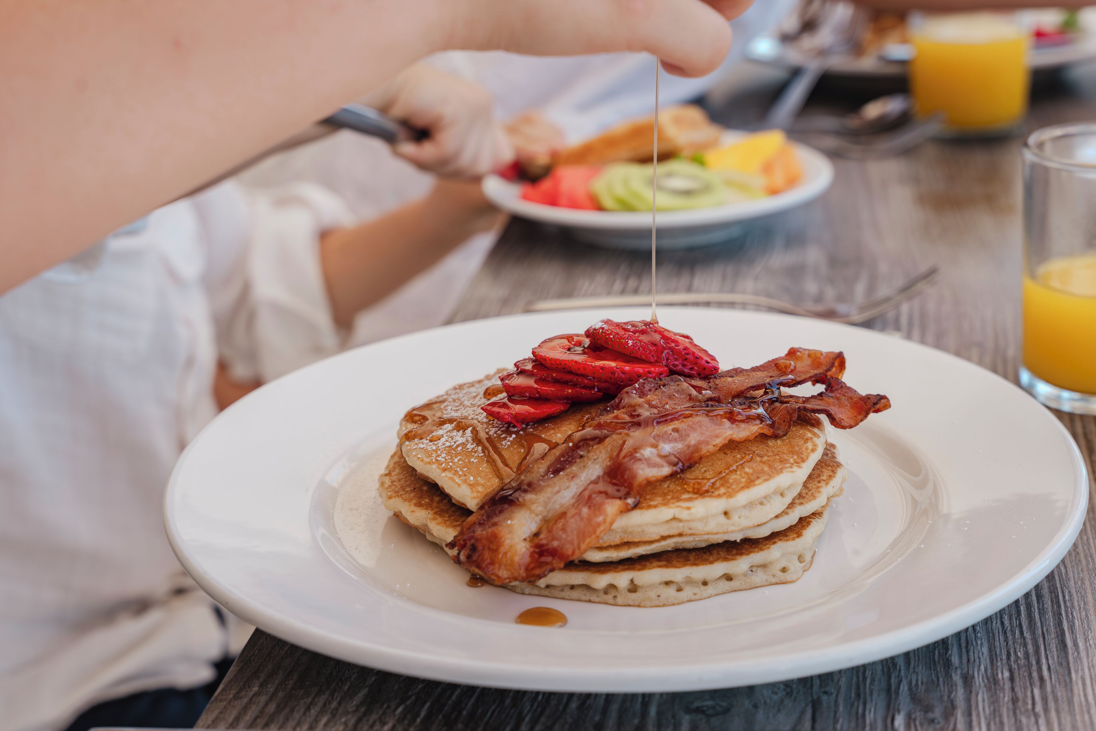 A breakfast plate with pancakes, strawberries, and bacon.