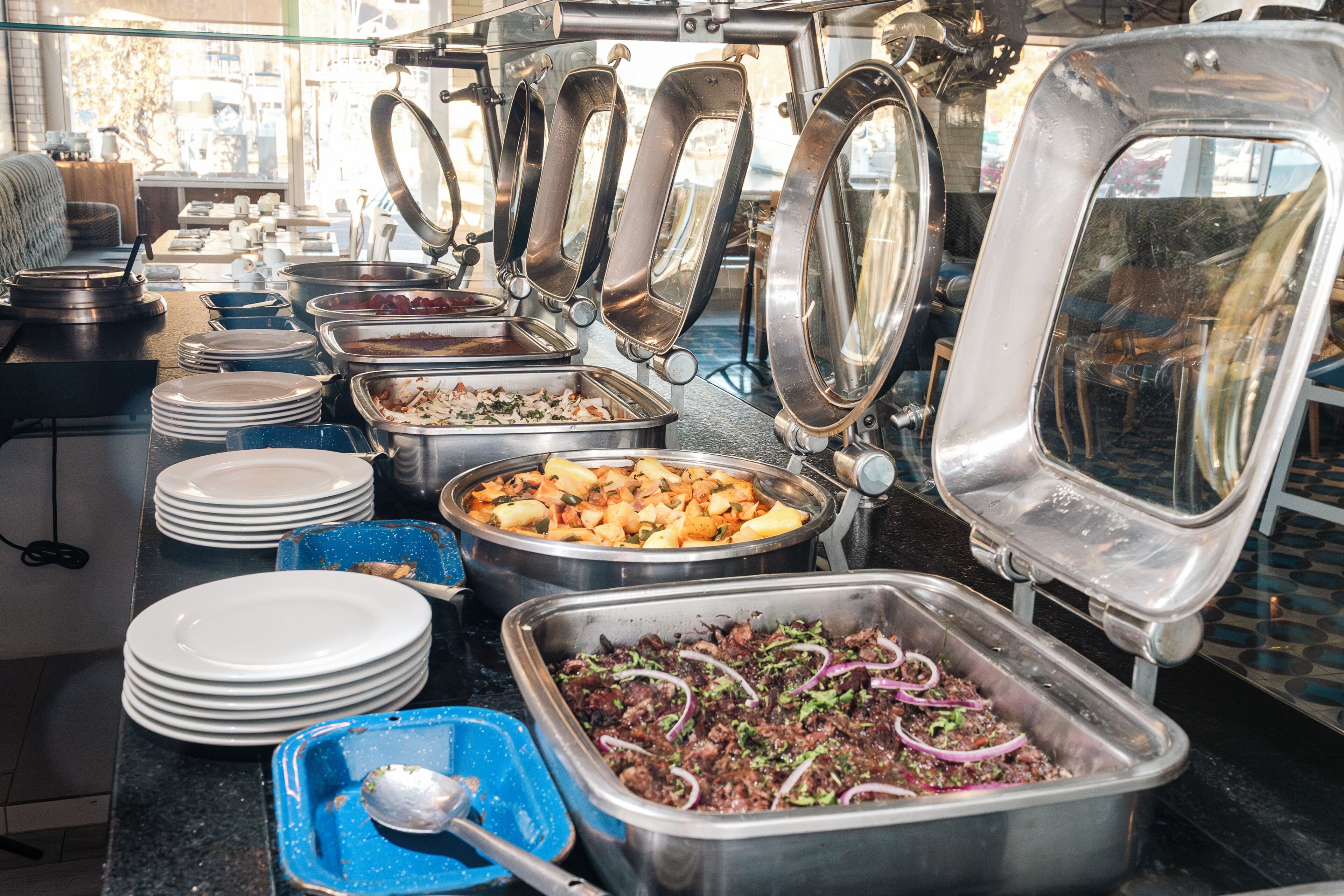 Una barra de buffet con diferentes recipientes de comida, platos y cubiertos.
