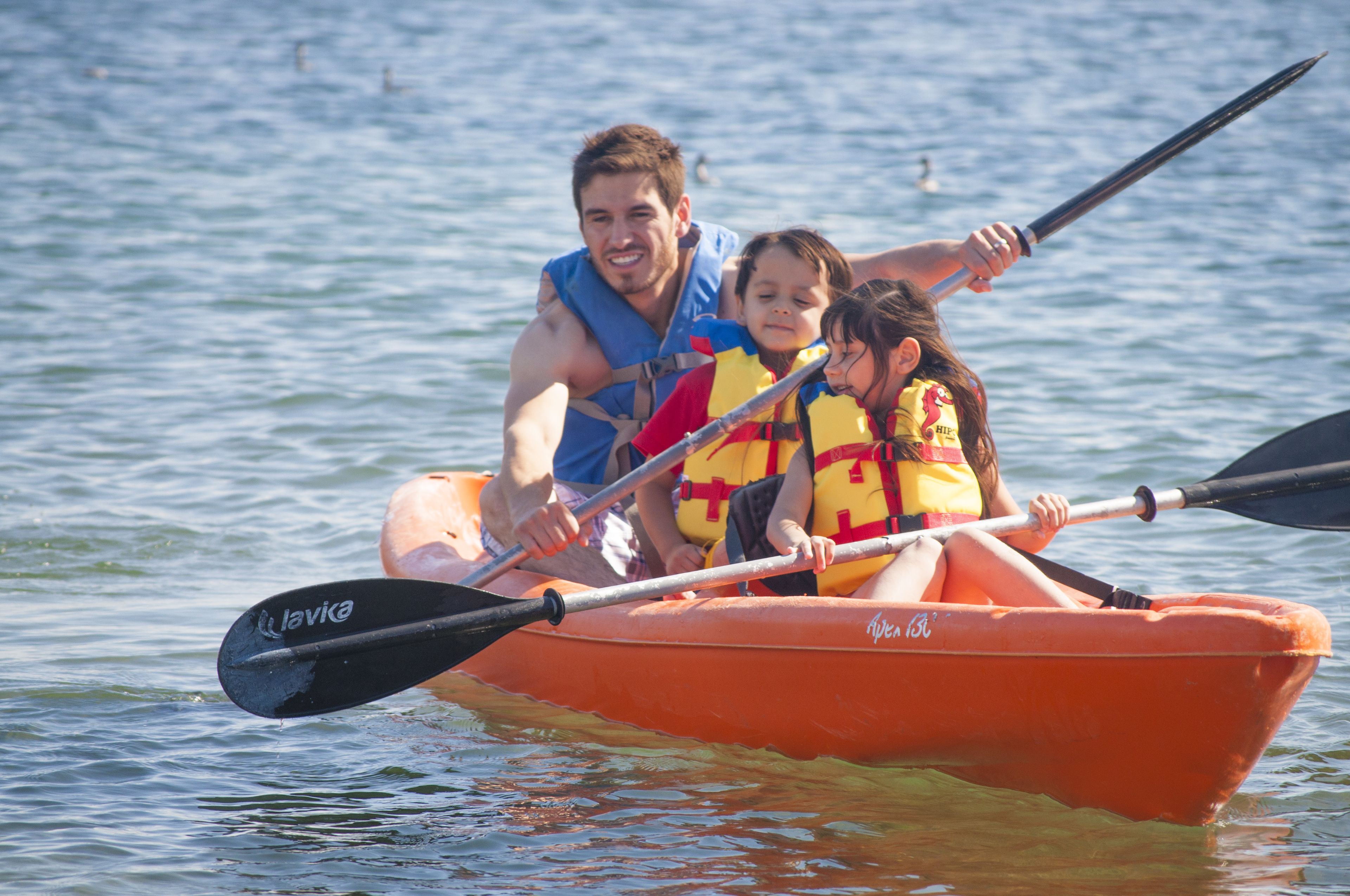 Una familia en un kayak naranja sobre aguas abiertas.