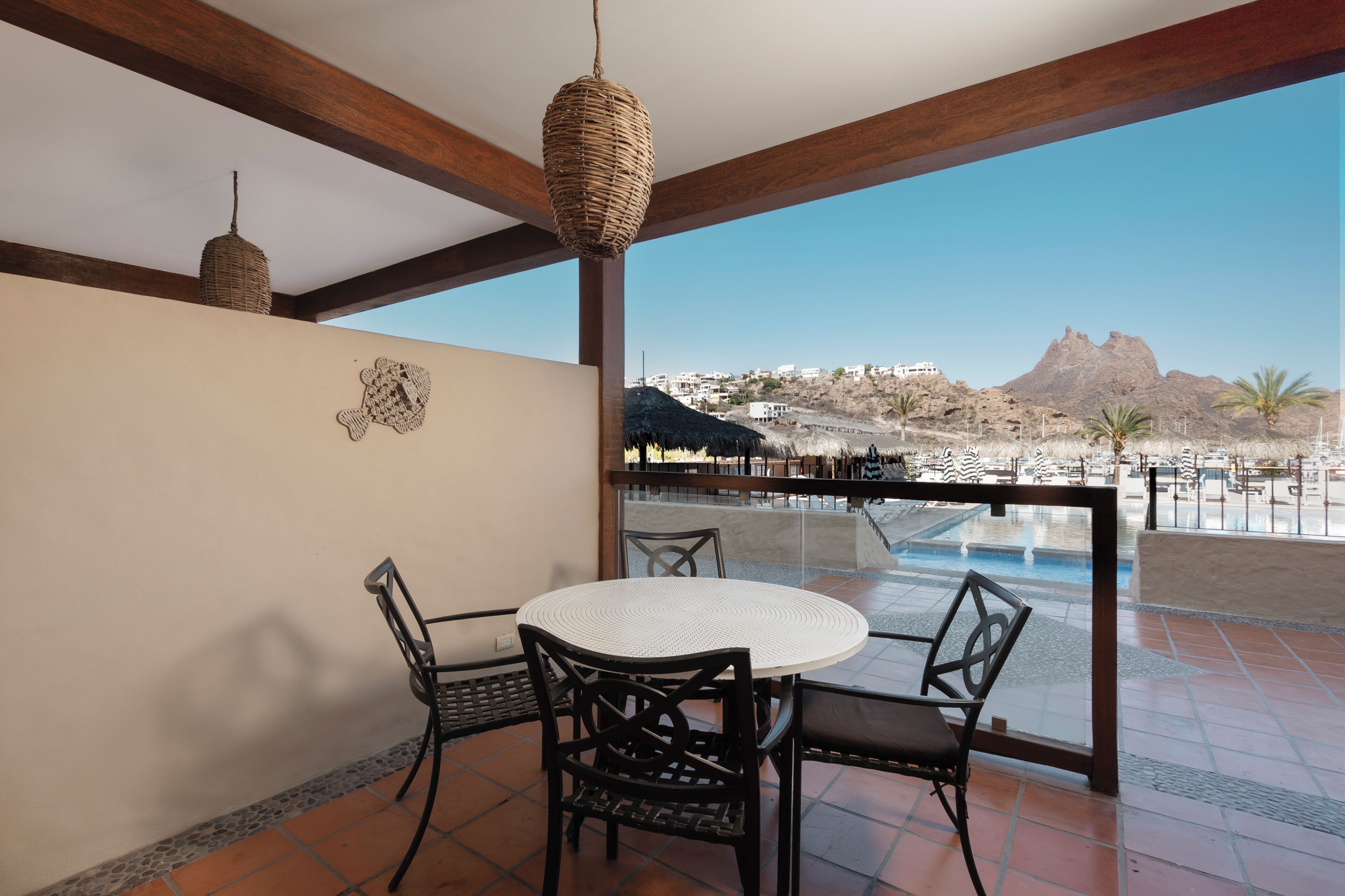 A balcony with a round table and chairs, a woven light fixture, and a view of a mountainous landscape.