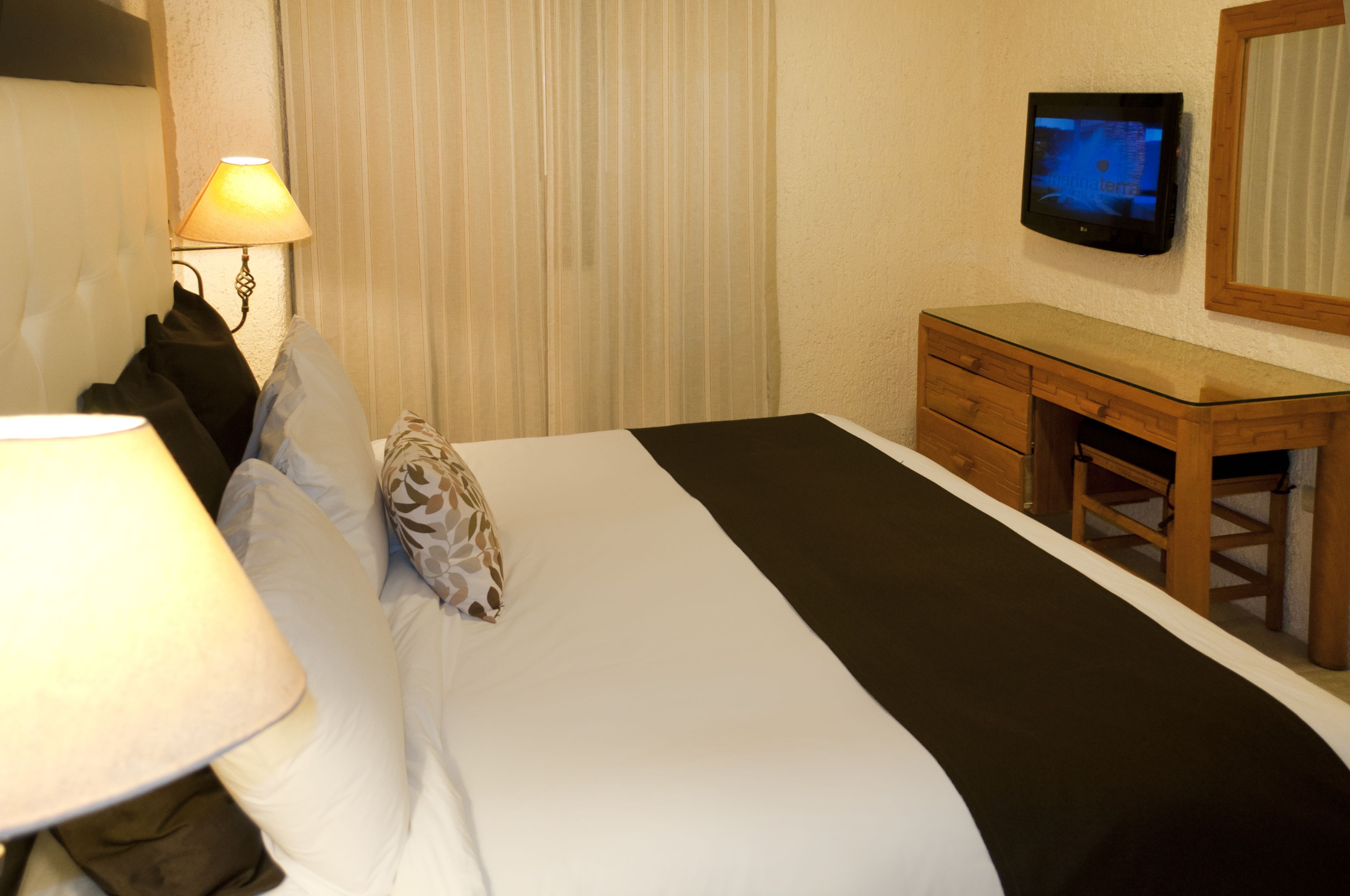 A hotel room with a bed, a bedside lamp, a TV, and a wooden dresser.
