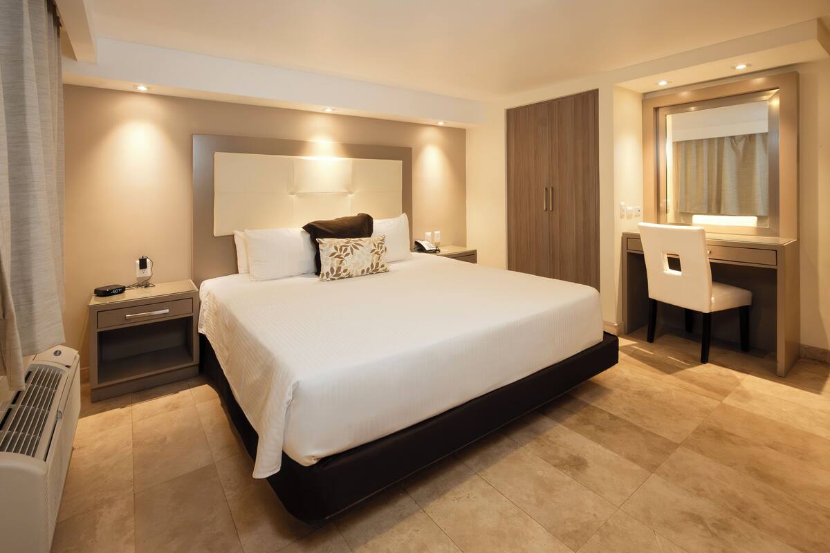 Una habitación de hotel con una cama grande, mesita de noche, escritorio, silla y un espejo.