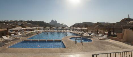Ein Poolbereich mit mehreren Pools, Liegestühlen und Sonnenschirmen.