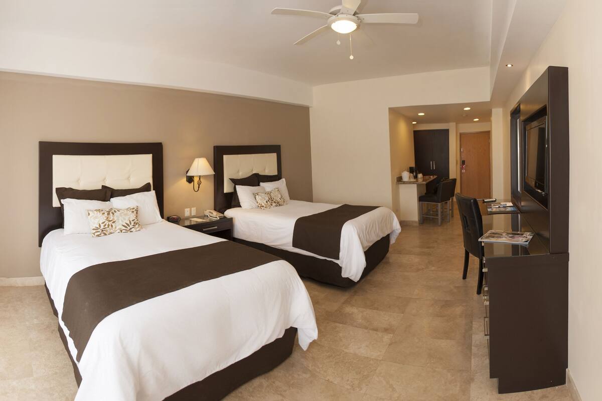 Habitación de hotel con dos camas, un escritorio, una silla, un televisor y un ventilador de techo.