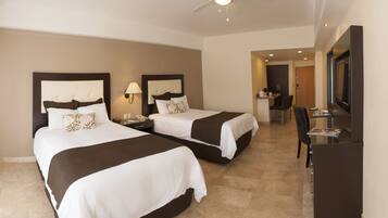 A hotel room with two beds, a desk, a chair, a TV, and a ceiling fan.