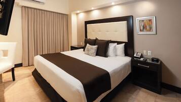 A hotel room with a large bed, a bedside table with a phone, a wall-mounted air conditioner, and a painting on the wall.