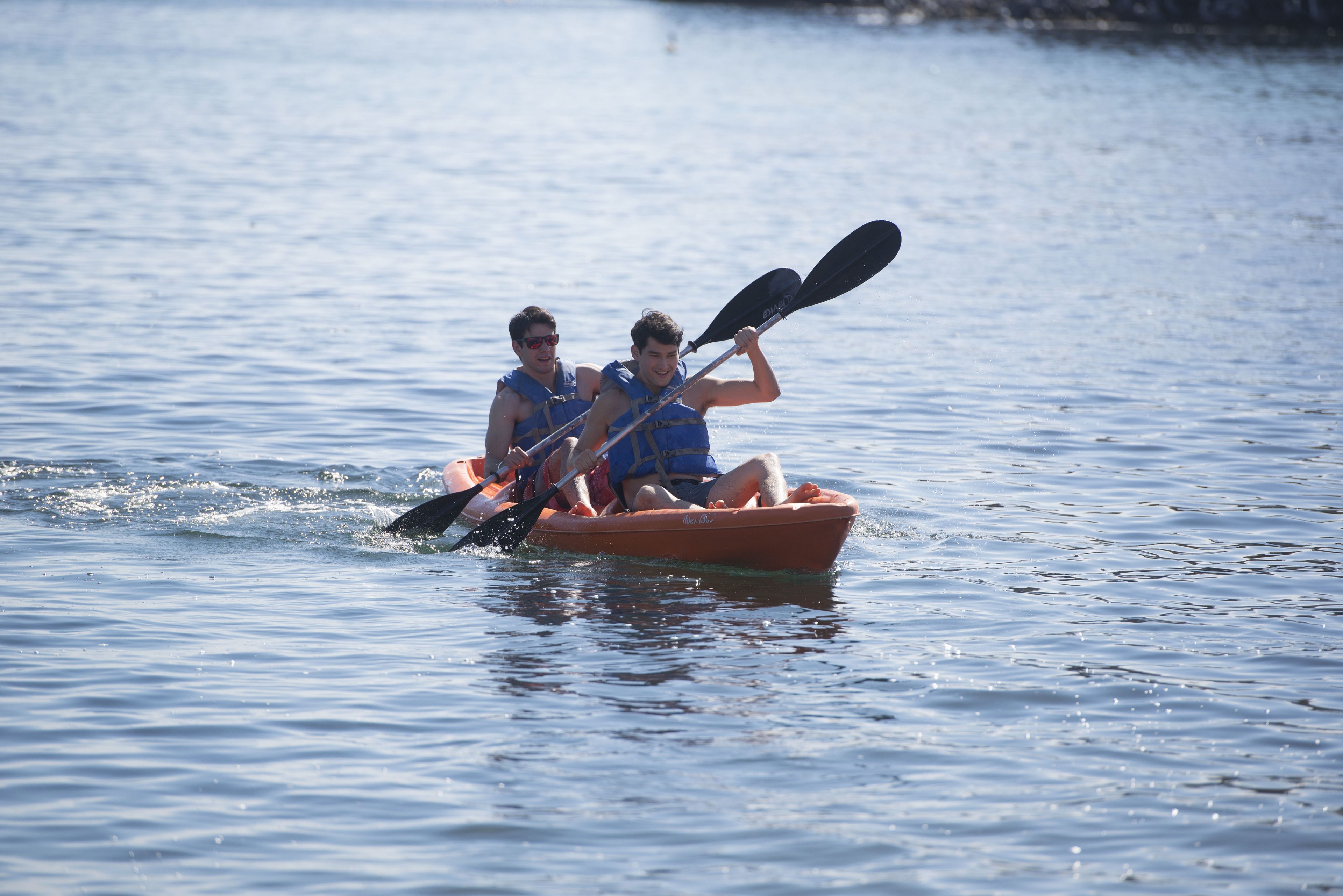 Two people in a small orange kayak on a calm body of water.