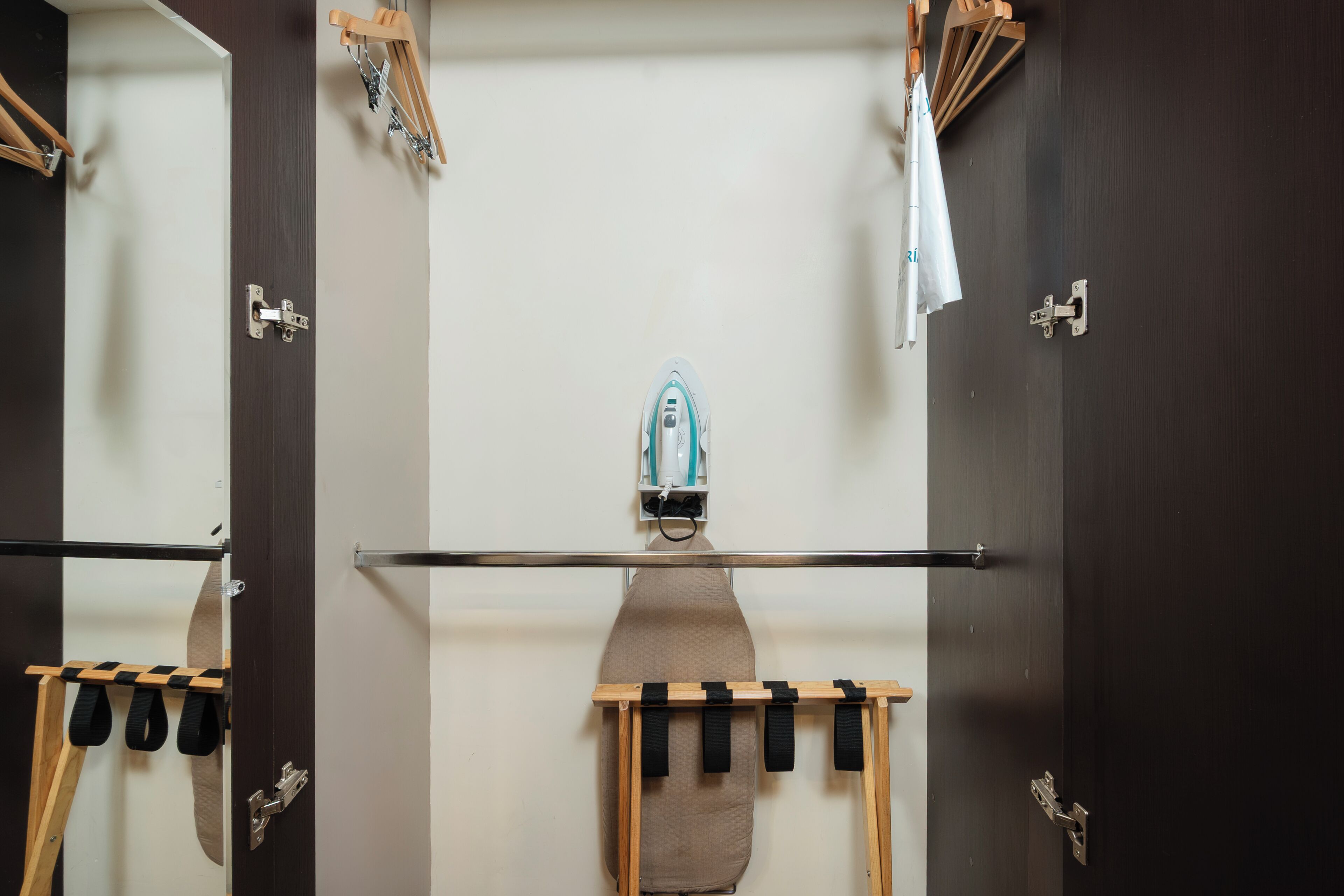 A room with a large mirror, a wooden ironing board, and a towel rack.