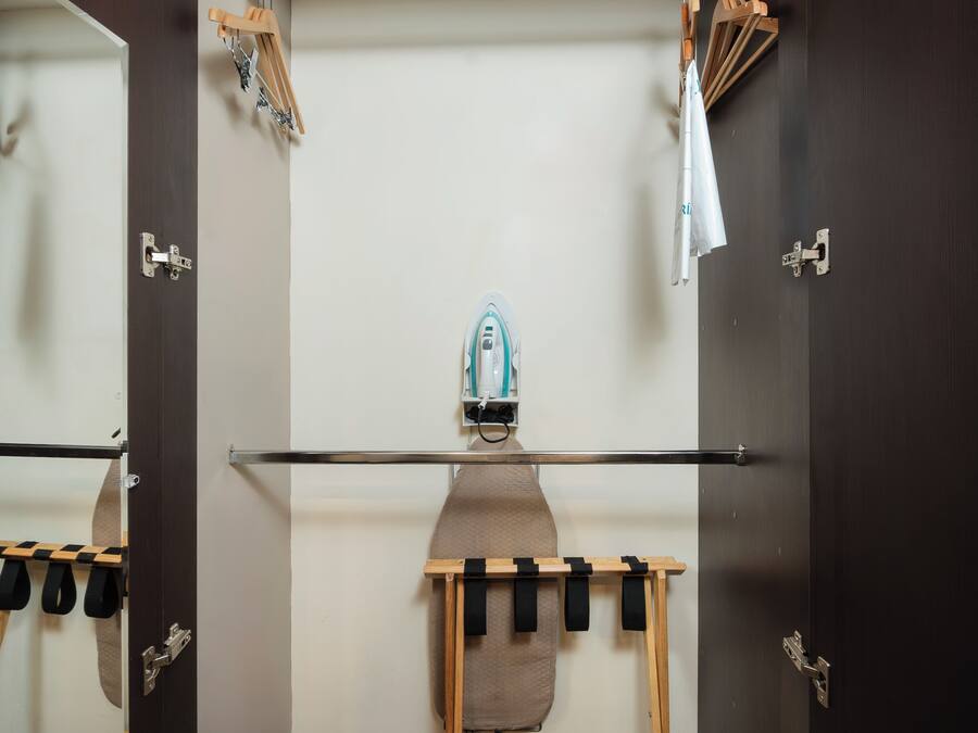 A room with a large mirror, a wooden ironing board, and a towel rack.
