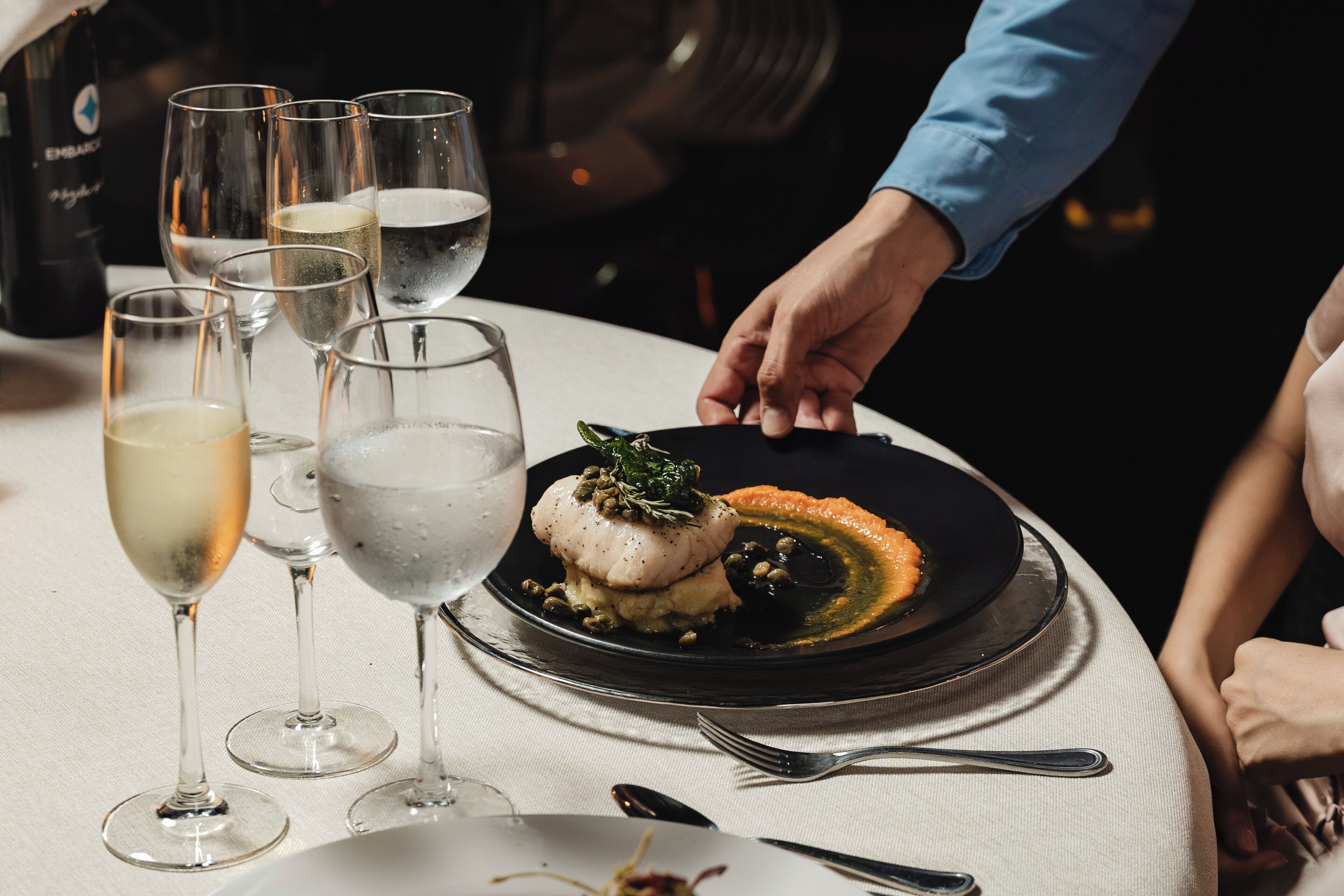 A table set with multiple glasses of champagne, a bottle of champagne, and a plate of food.