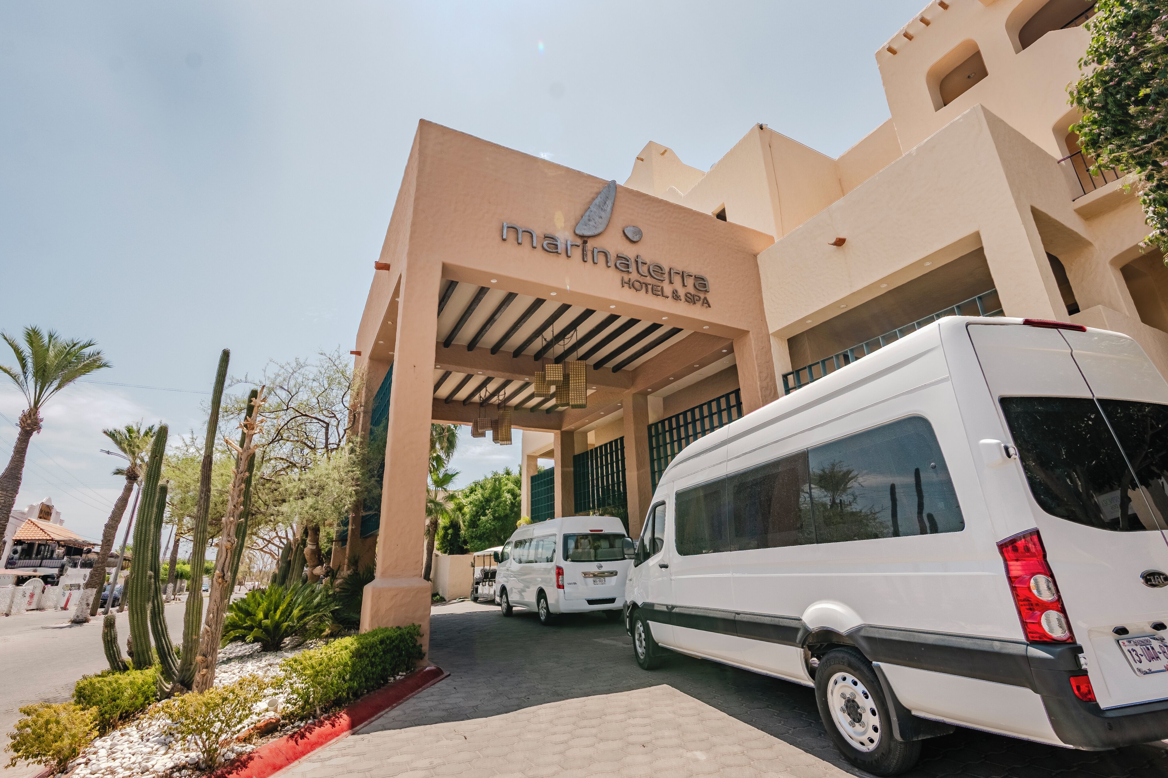 Entrada de un hotel con un cartel que dice 'Marinaterra Hotel & Spa', una camioneta blanca estacionada frente y un jardín de cactus.