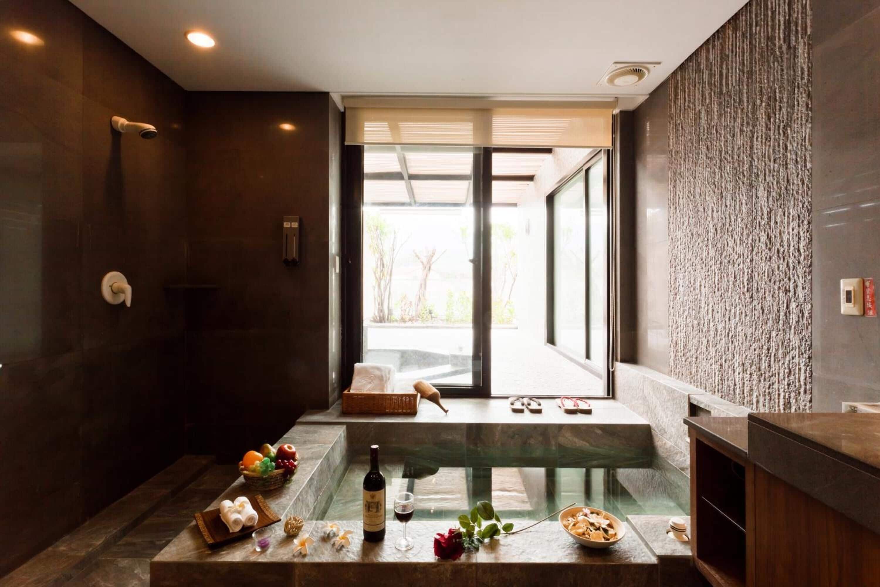 A modern bathroom with a glass-enclosed jacuzzi, a wooden vanity, and a view of the outdoors.